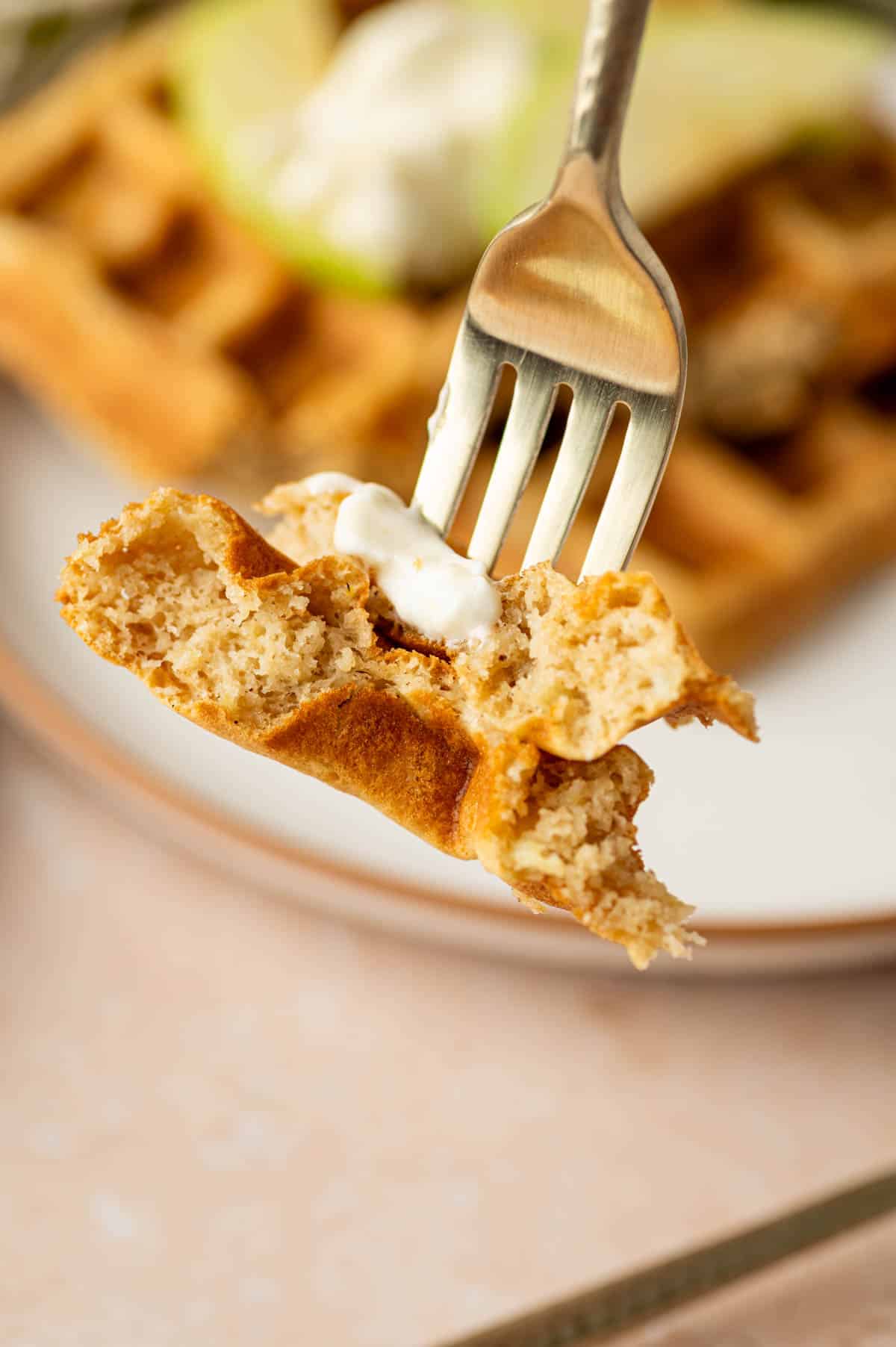 Close-up of crispy waffles with grated apple and cinnamon in a fork showing inside part.