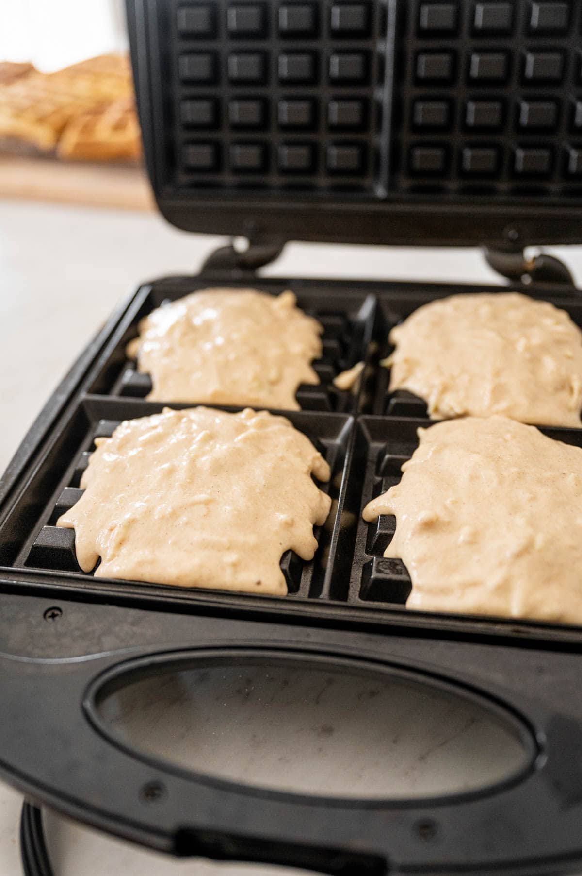 Batter being poured in the waffle maker to make apple waffles.