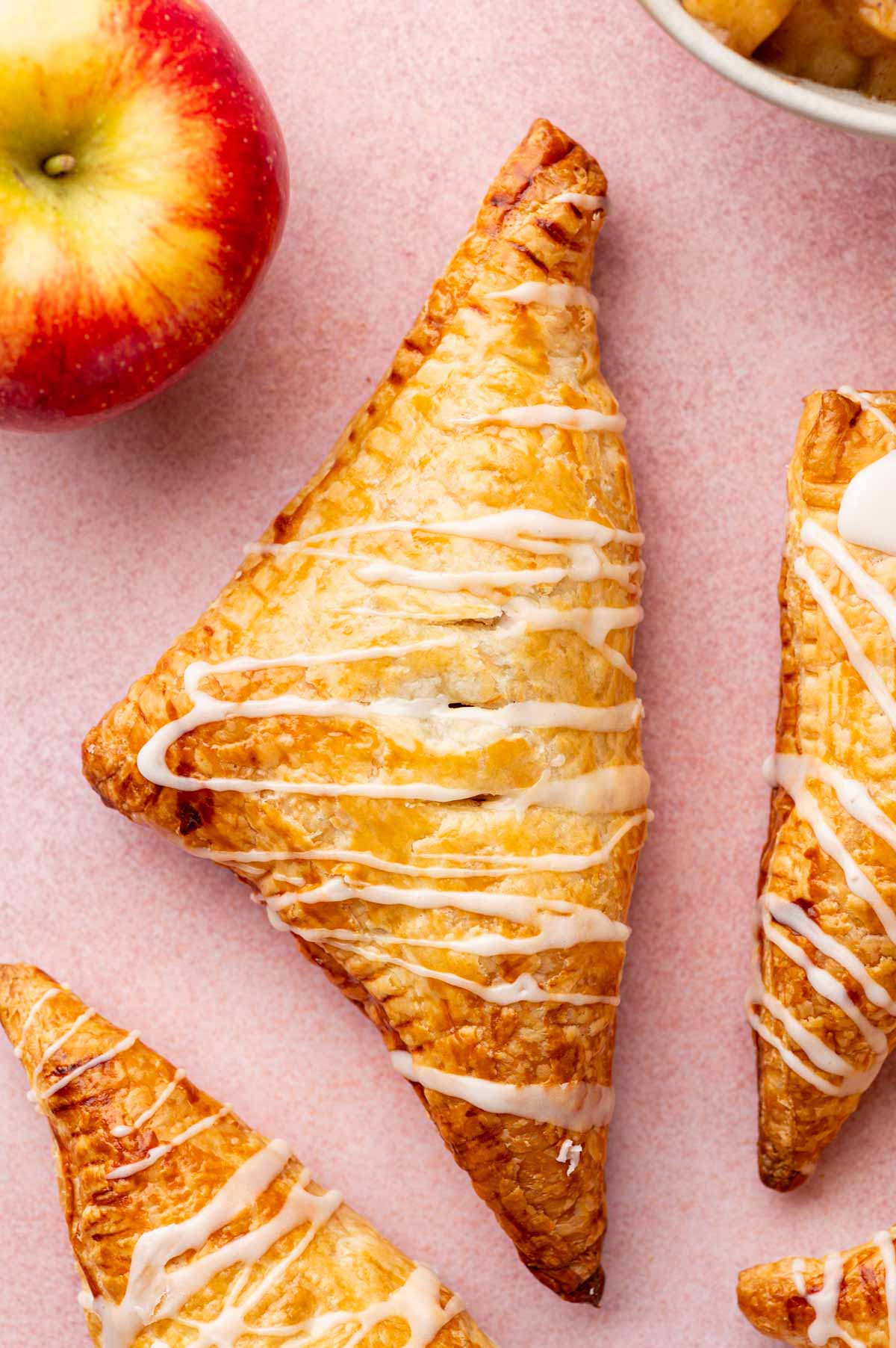 A single Flaky apple turnovers on a pink background with cinnamon apple filling in it.