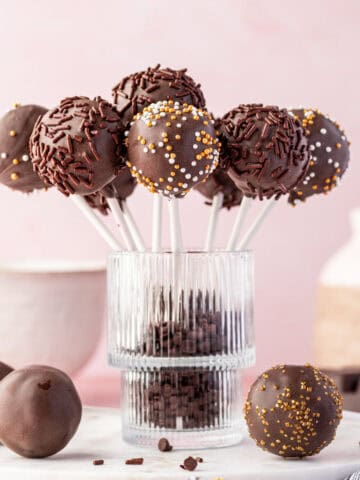 Brownie cake pops with festive drizzle and sprinkles displayed upright with sticks.