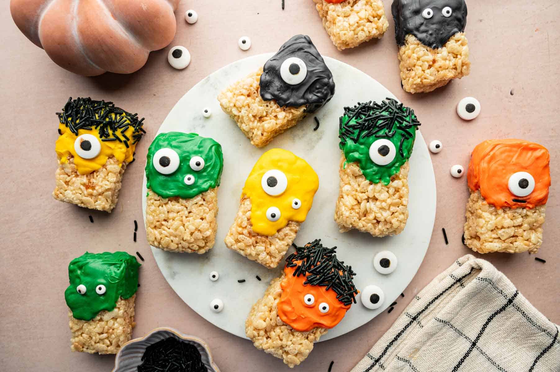 Spooky Halloween Rice Krispie Treat squares topped with festive sprinkles and candy googly eyes on a white marble.