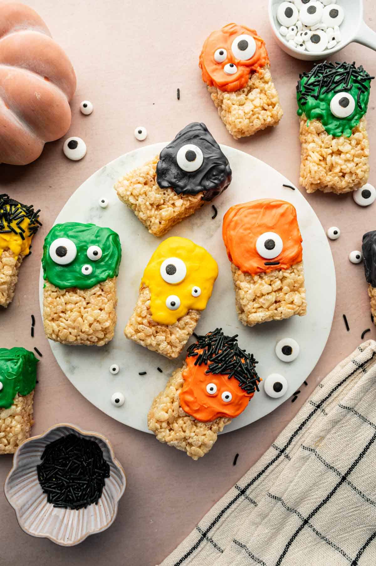 Spooky Halloween Rice Krispie Treat squares topped with festive sprinkles and candy googly eyes on a white plate.