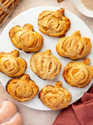 Mini pumpkin-shaped hand pies with a golden crust, arranged on a marble plate.