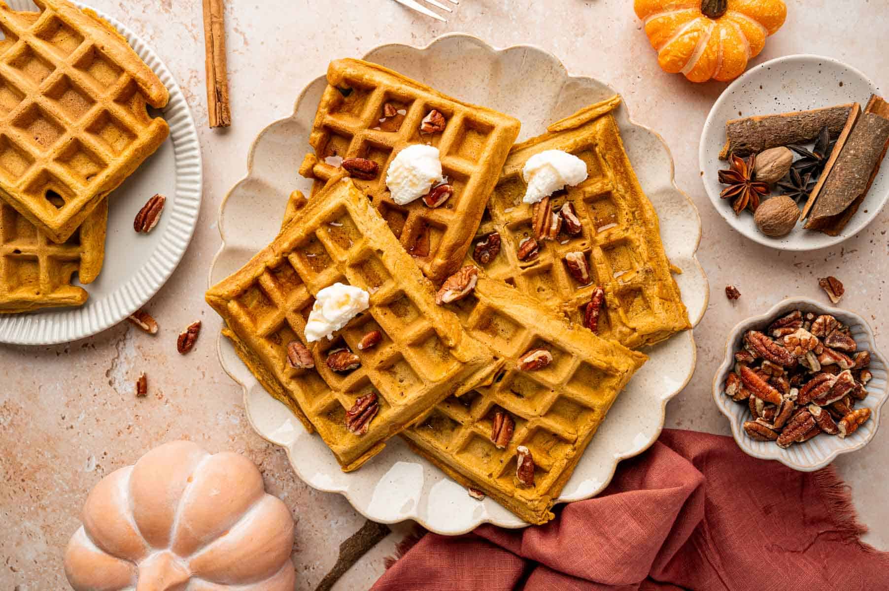 Overhead shot of pumpkin pecan waffle served in a platter topped with pecans, whipped cream and maple syrup.