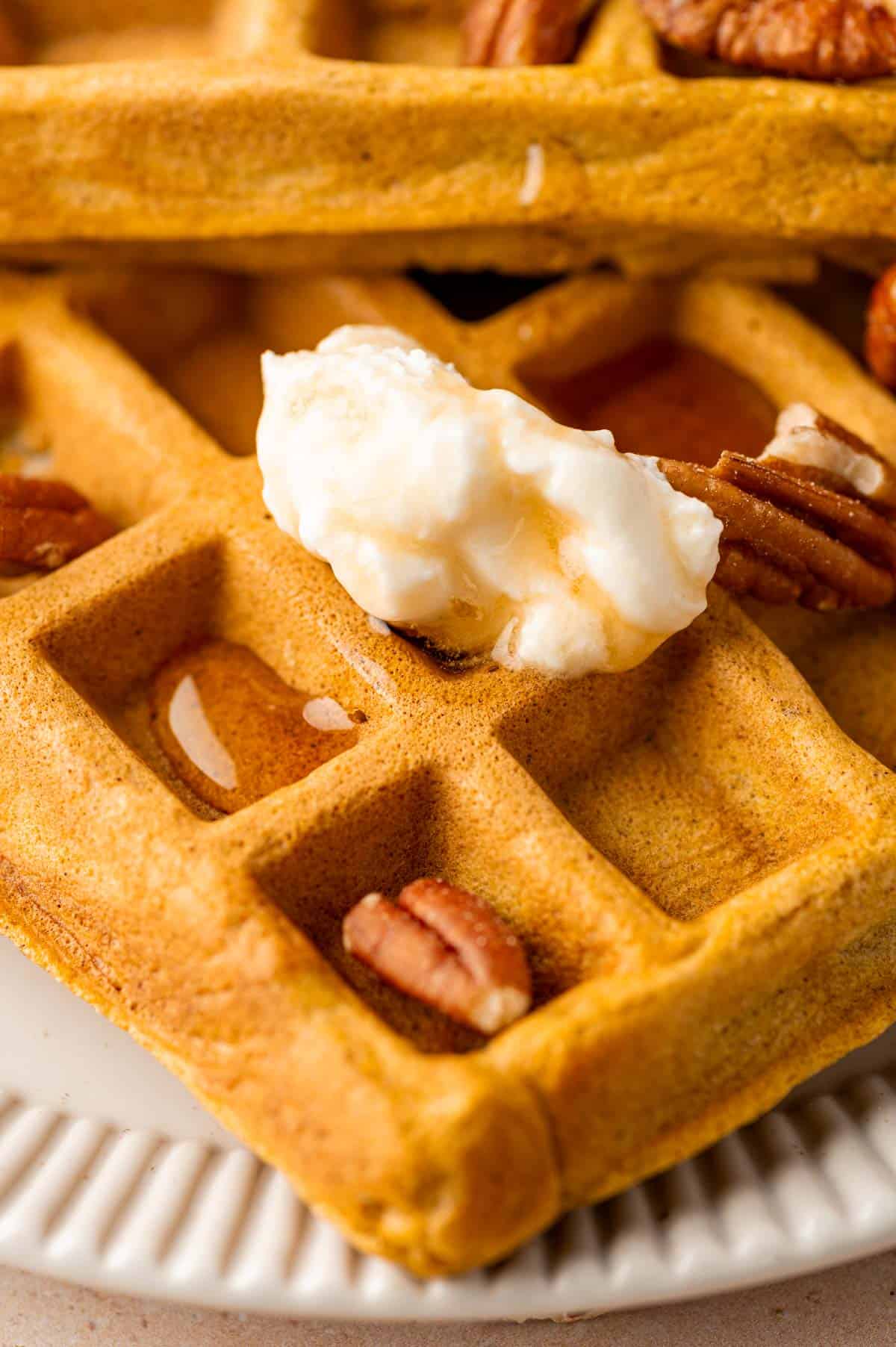 Close-up of fluffy pumpkin waffles with chopped pecans top of the waffles.