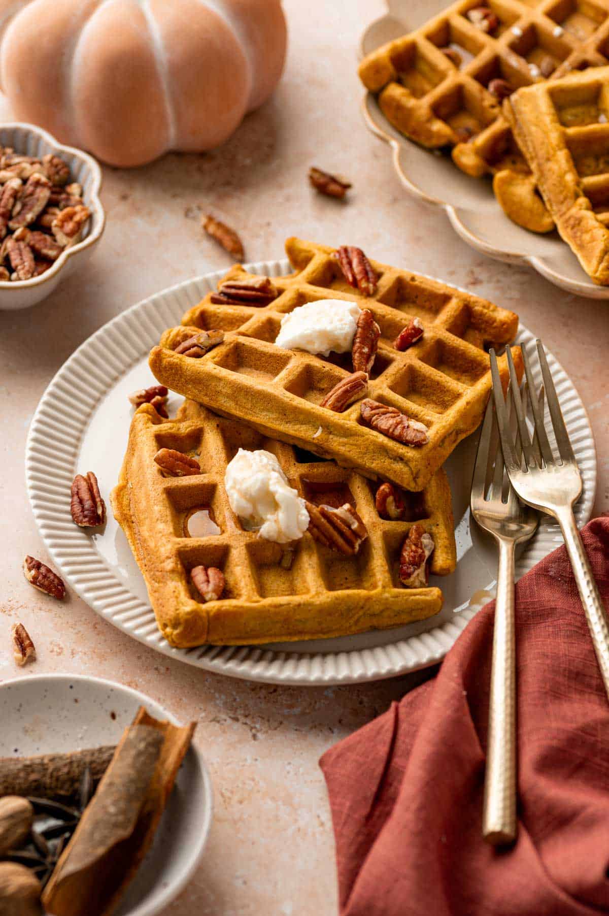 Golden brown pumpkin pecan waffles on a plate with whipped cream and cinnamon in a plate.