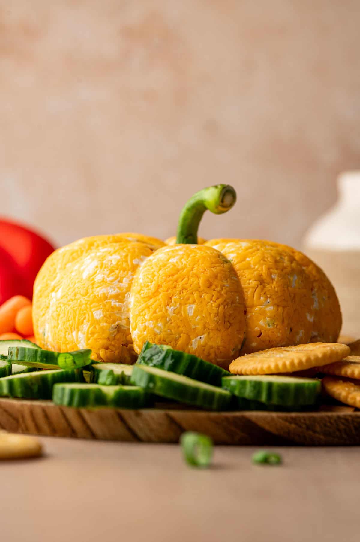 Creamy cheese ball molded into a pumpkin shape, topped with a bell pepper stem and ready for a Halloween party.