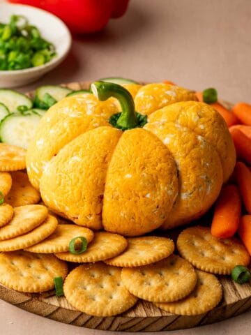 A festive pumpkin-shaped cheese ball coated in cheddar cheese, served on a platter with crackers.