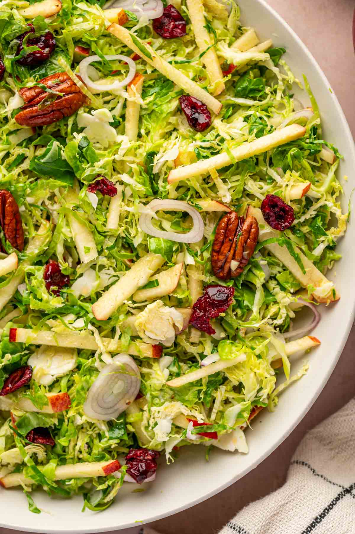 In a white bowl, Crisp Brussels sprouts salad with apples and maple dressing, perfect fall side dish.