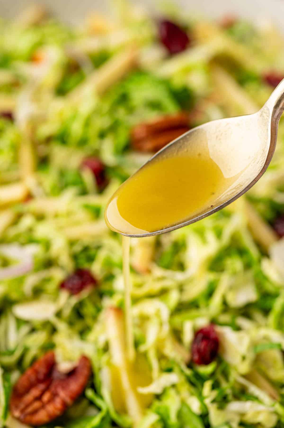 Close-up shot of maple Dijon dressing in spoon being poured over the salad.