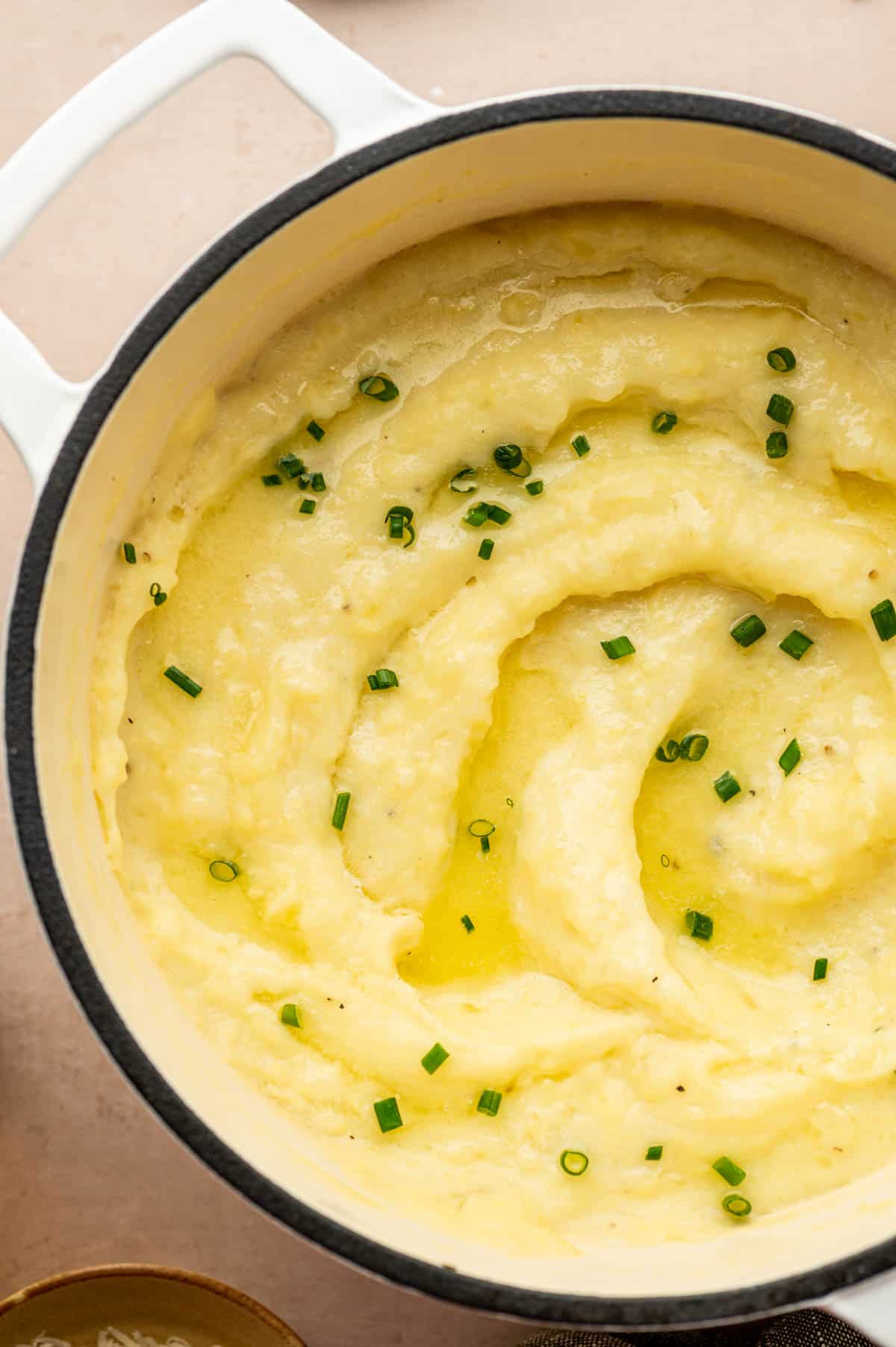 Creamy mashed potatoes topped with cheese, garnished with fresh chives in a white dutch oven.