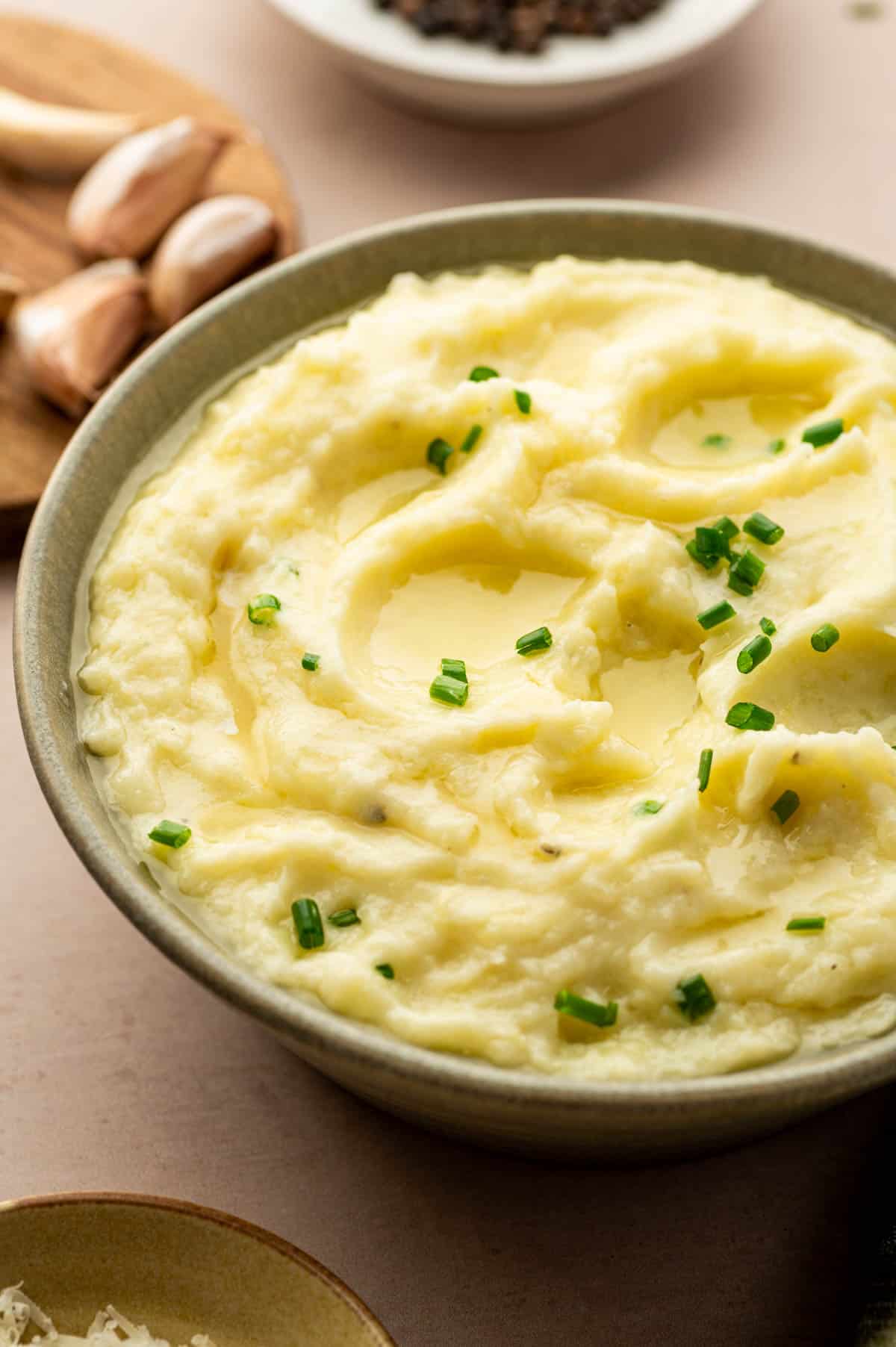 Creamy and cheesy mashed potatoes, a ultimate thanksgiving side dishes placed in a green bowl, garnished with chives.