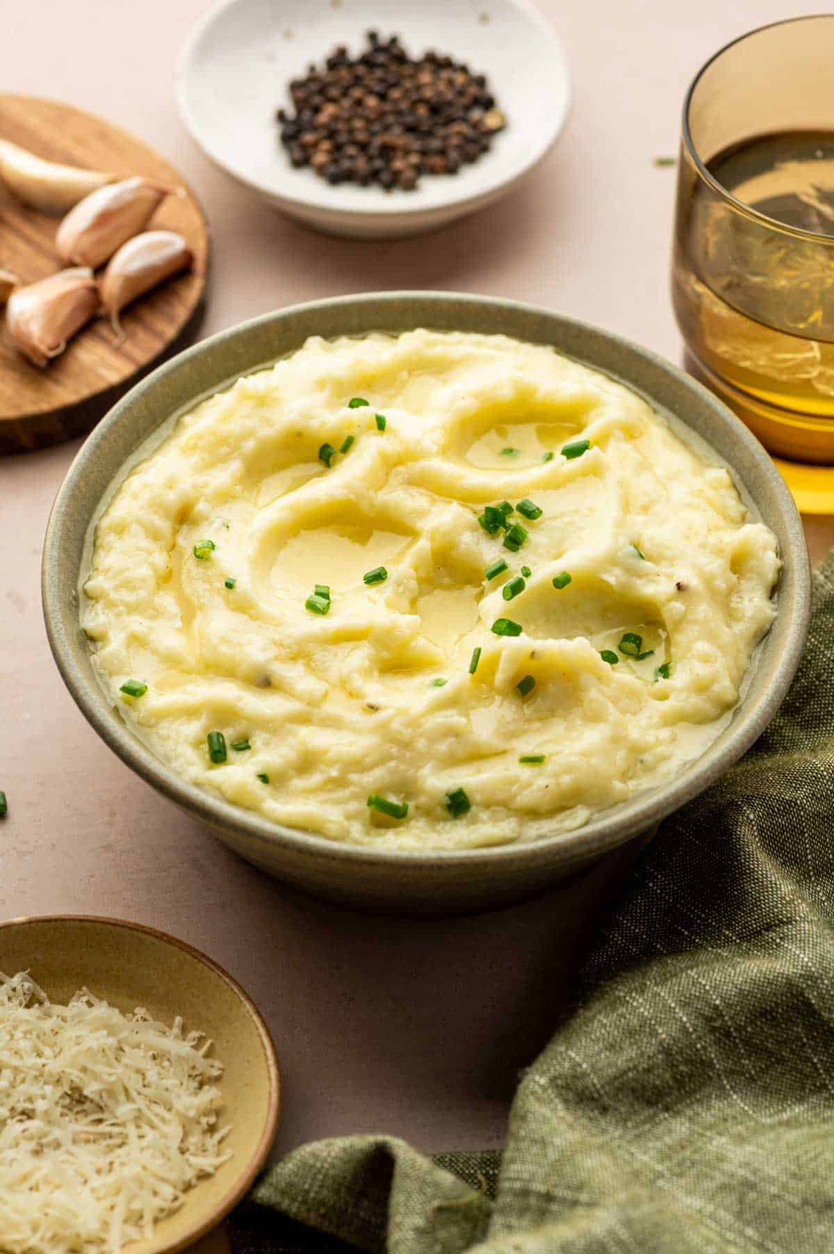 Creamy mashed potatoes topped with melted cheese, garnished with fresh chives in a rustic green bowl.