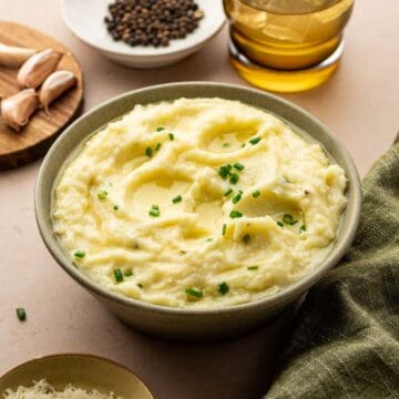 Creamy mashed potatoes topped with melted butter, garnished with fresh chives in a rustic green bowl.
