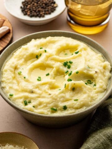 Creamy mashed potatoes topped with melted butter, garnished with fresh chives in a rustic green bowl.