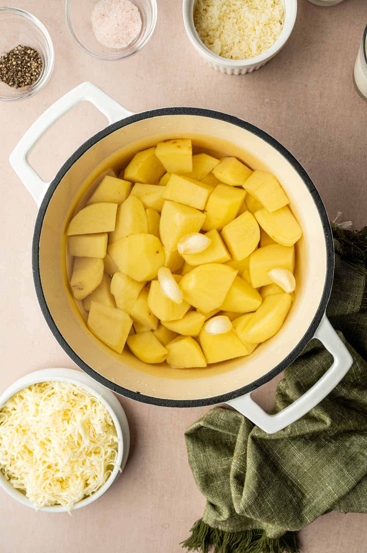 In a white dutch oven, potatoes are boiling along with garlic to make mashed potatoes.