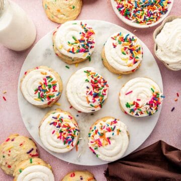 Frosted funfetti birthday cookie on marble top with extra sprinkles scattered.