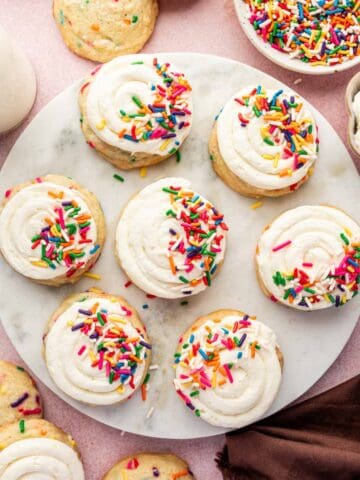 Frosted funfetti birthday cookie on marble top with extra sprinkles scattered.