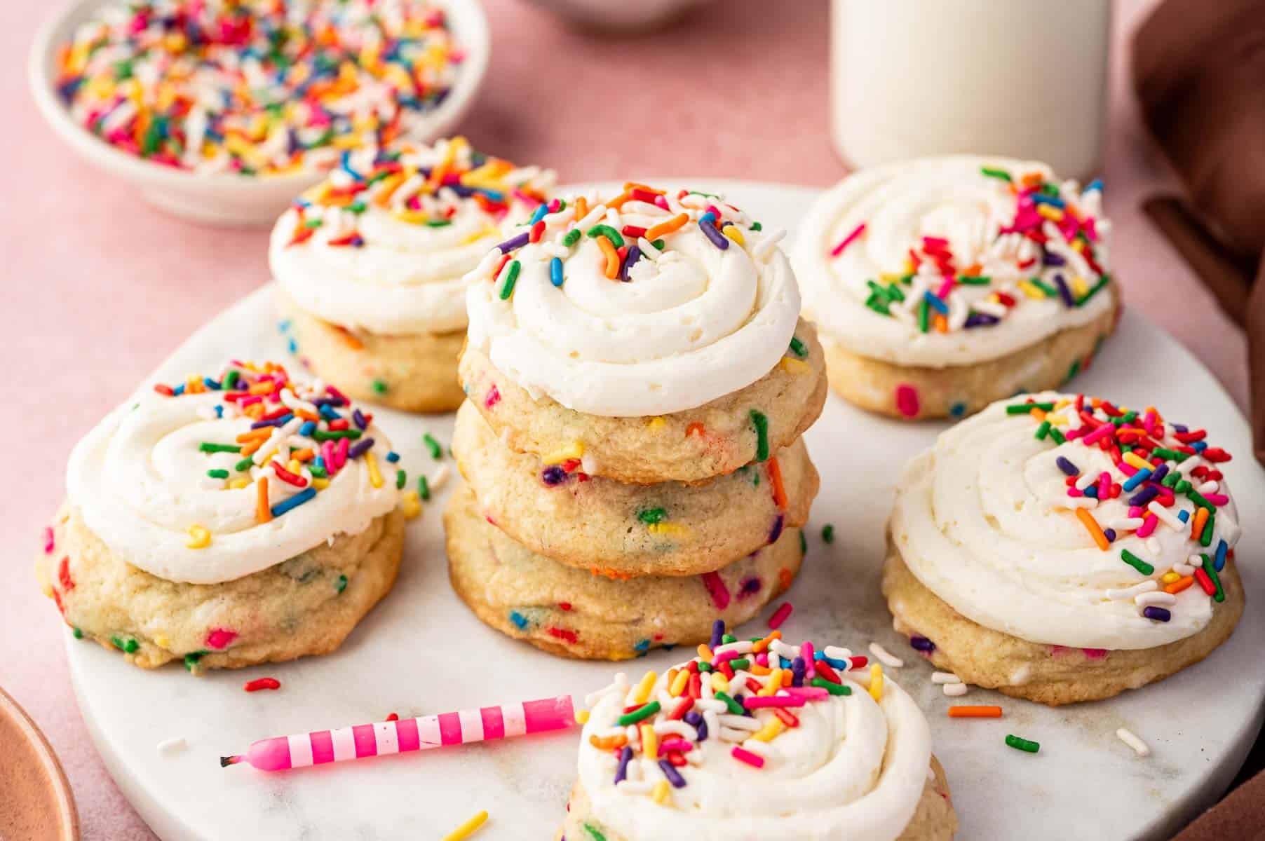 Frosted funfetti birthday cookie on parchment with extra sprinkles scattered.