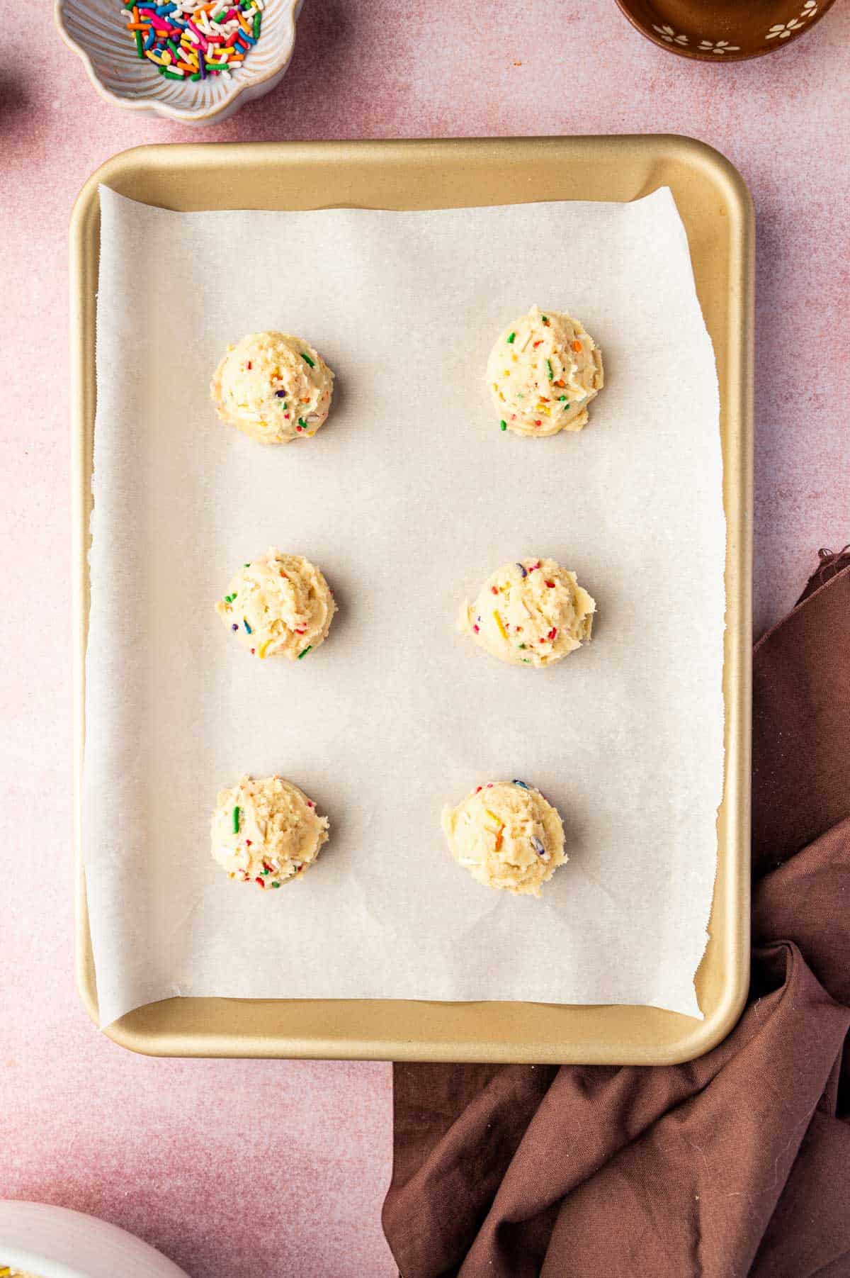Cookie scoop portioning funfetti dough onto lined baking sheet.