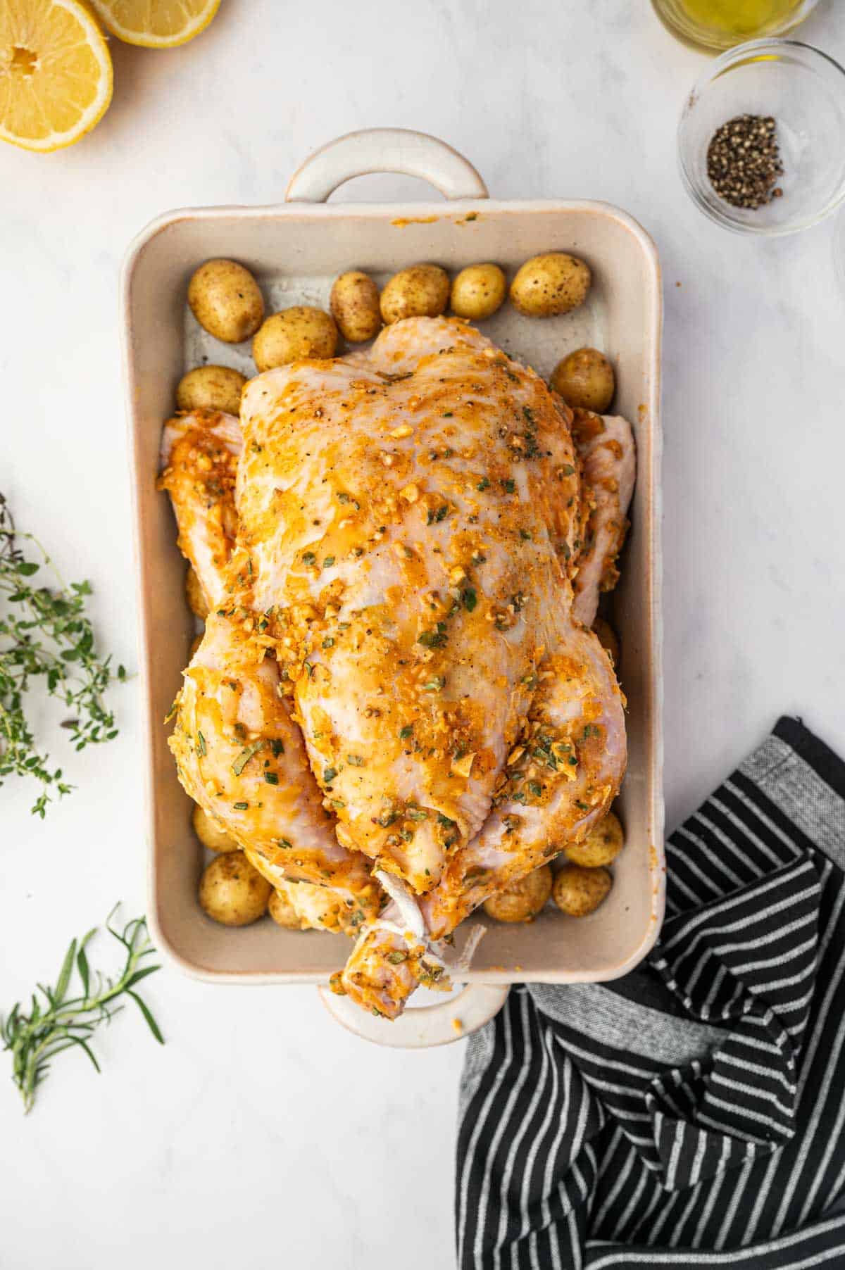 Whole chicken and potatoes are seasoned and ready to bake in the oven.