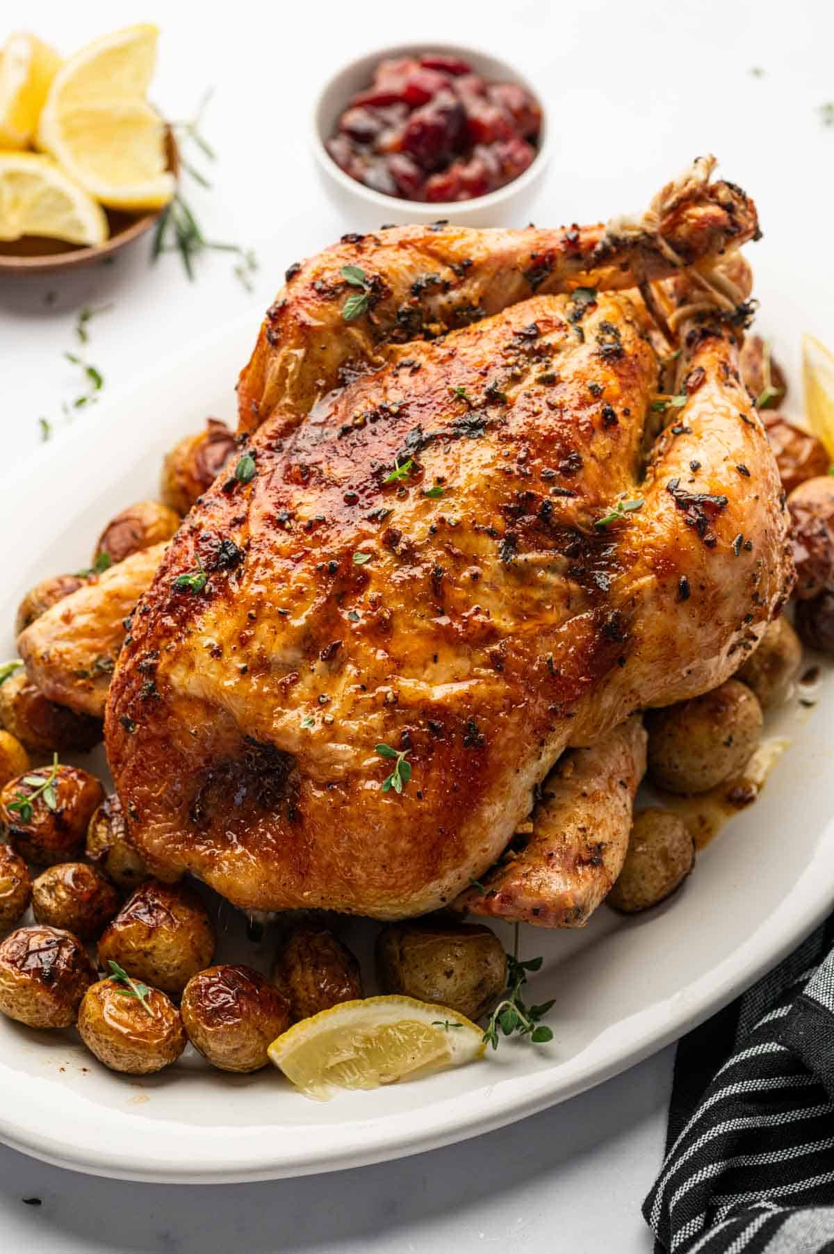 Oven roasted whole chicken with golden baby potatoes, garlic, and herbs in a serving platter.
