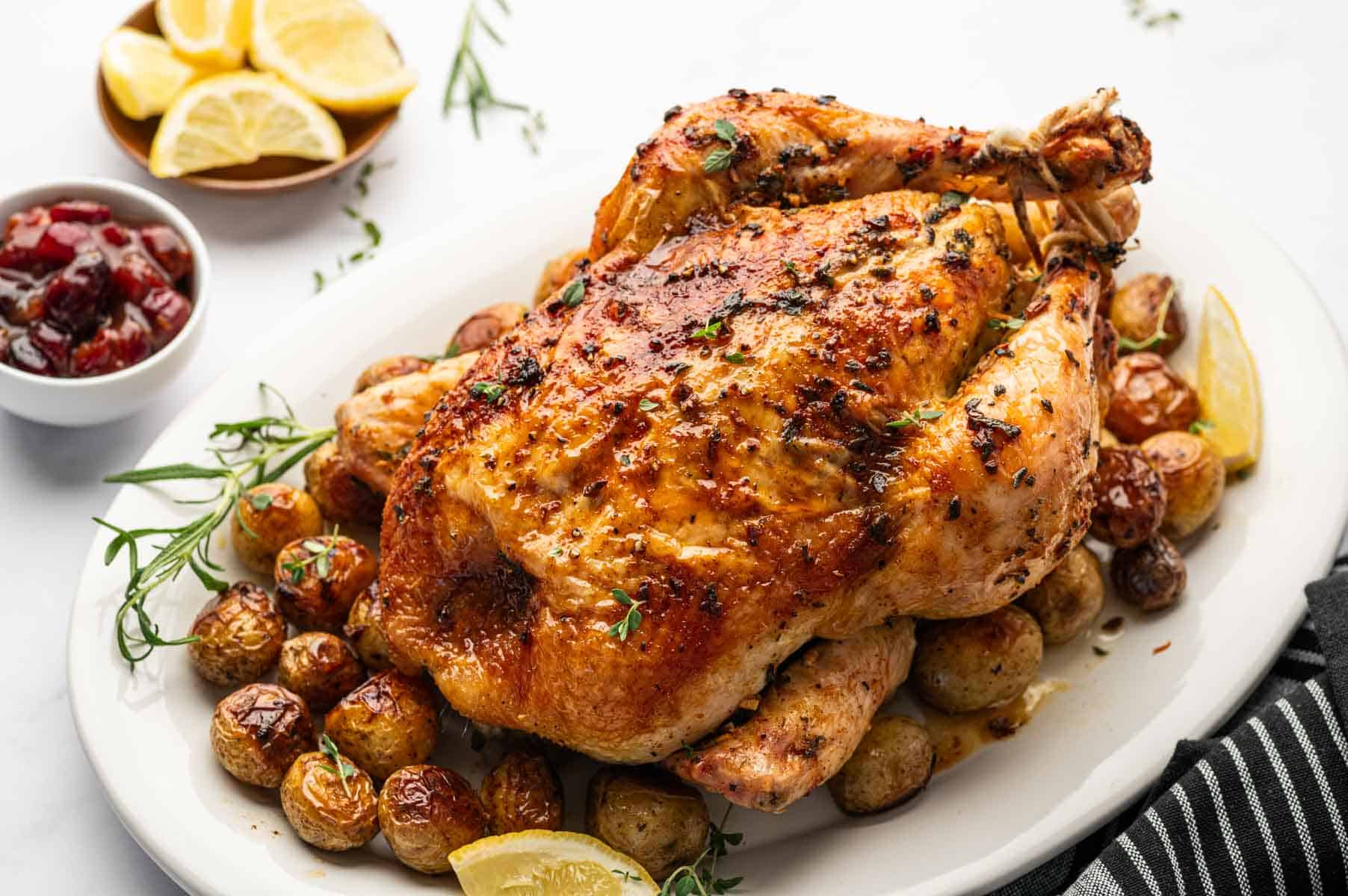 Whole roasted chicken surrounded by roasted baby potatoes and fresh herbs.