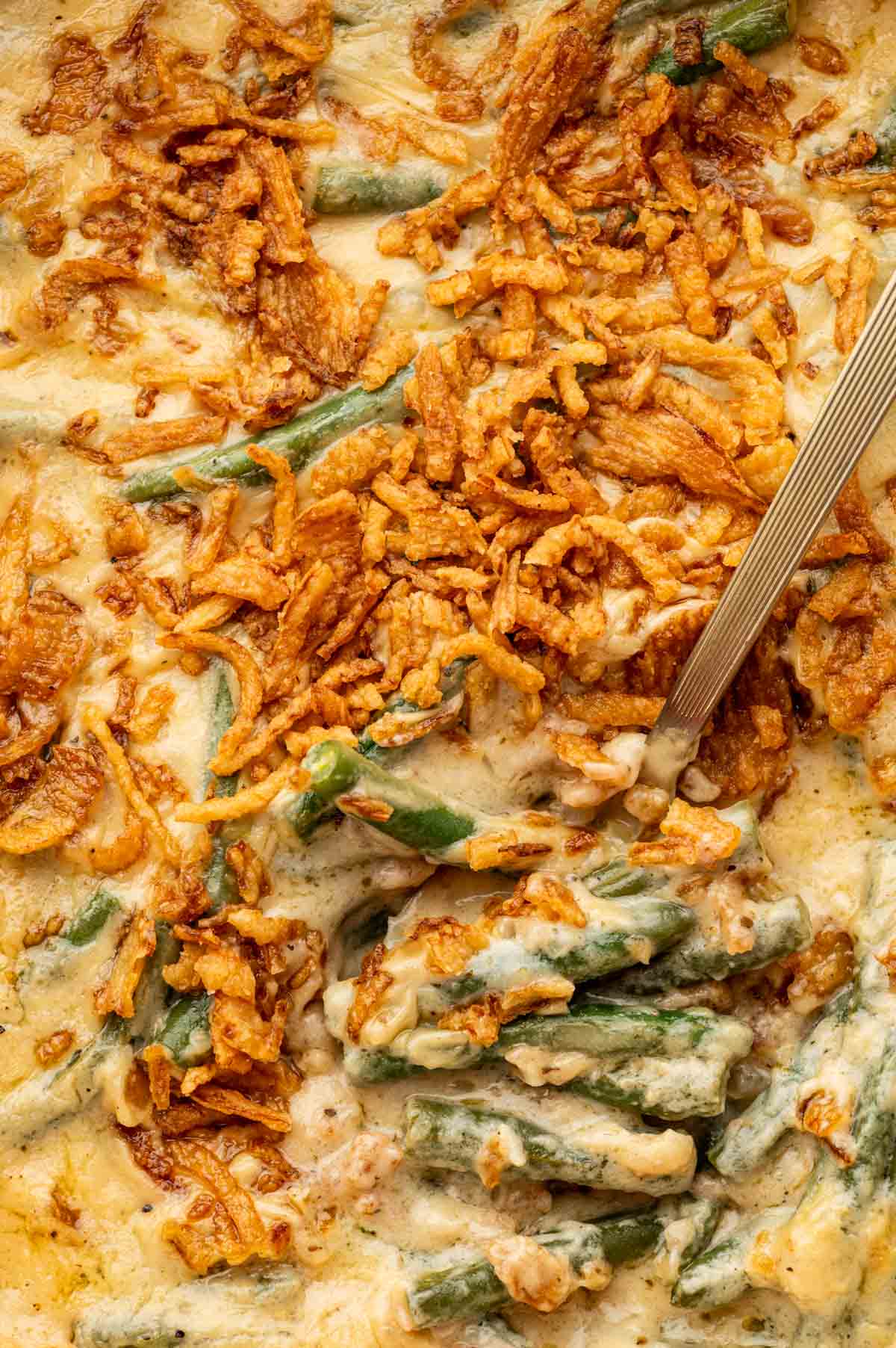 Top angle shot of creamy cheese green bean casserole without mushroom soup, a spoon being ready to scoop.