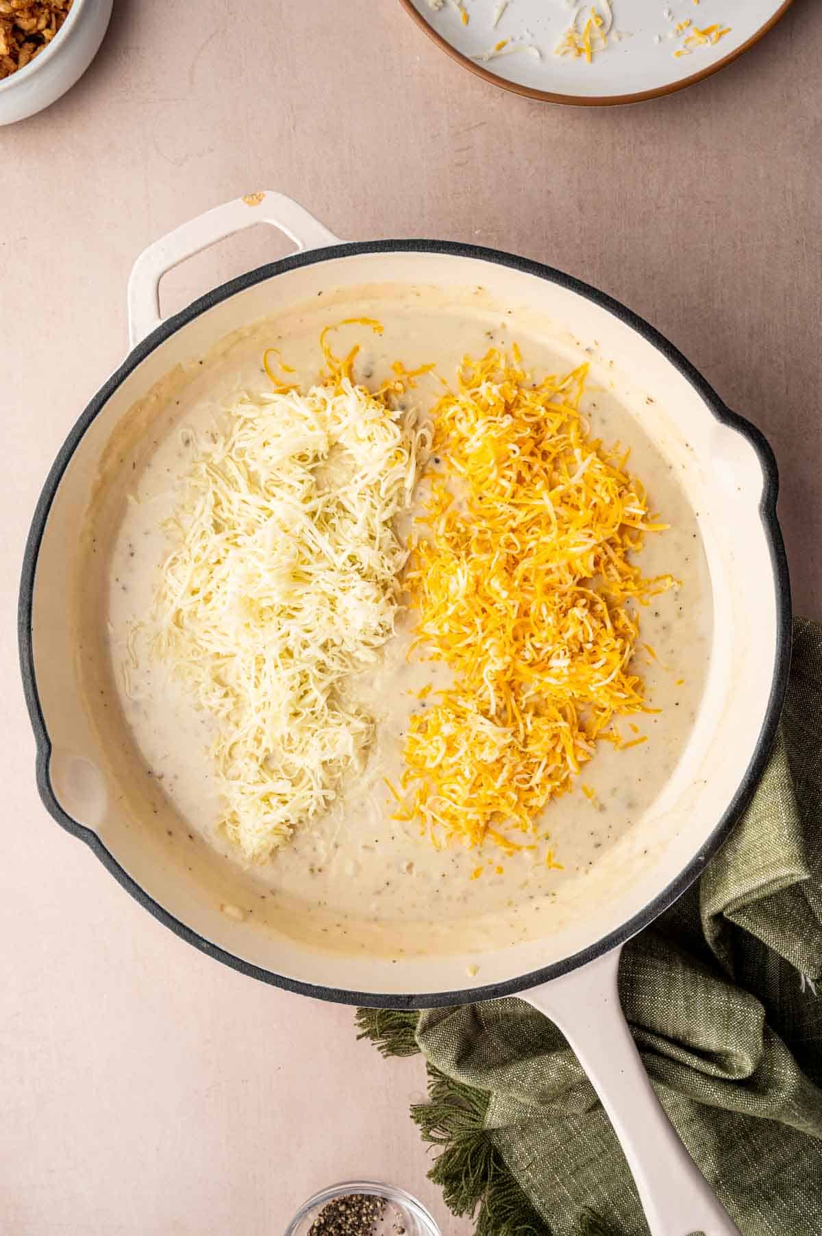 Two types of cheeses being added to the sauce.