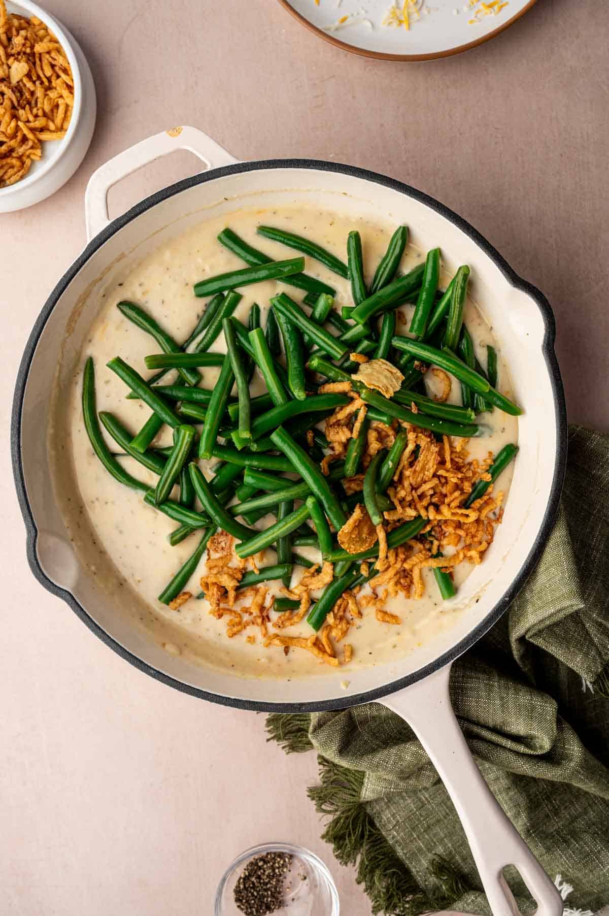 Blanced green beans and crispy fried onions being added to the cheesy sauce.