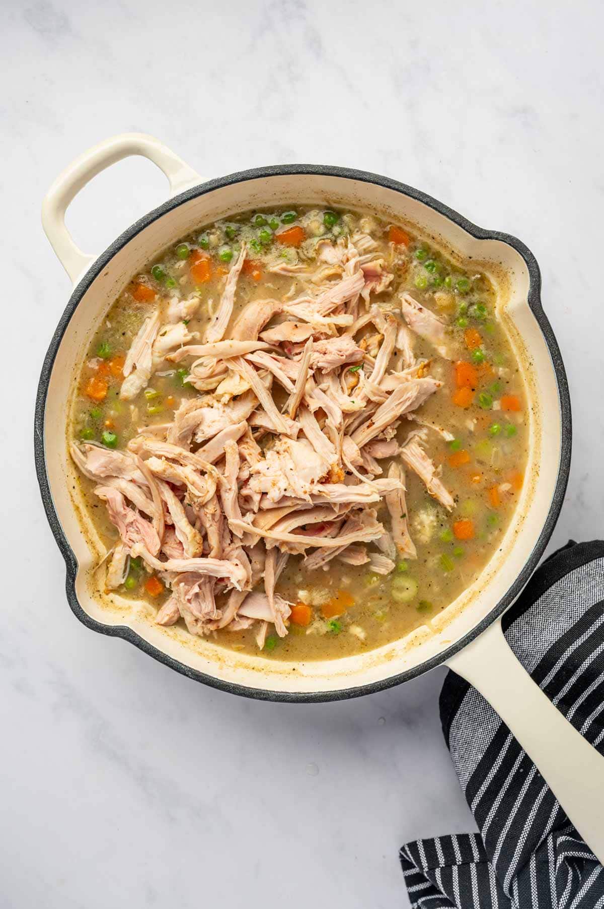 Shredded chicken being added to the skillet.