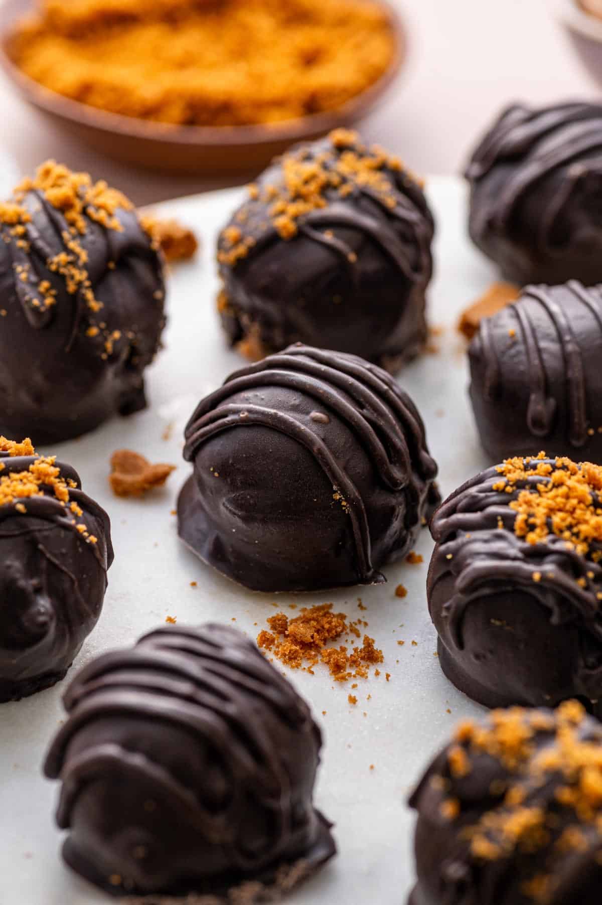 Close-up of creamy Biscoff truffles coated in glossy dark chocolate, sprinkled with crushed Lotus Biscoff cookies on top decorated beautifully.