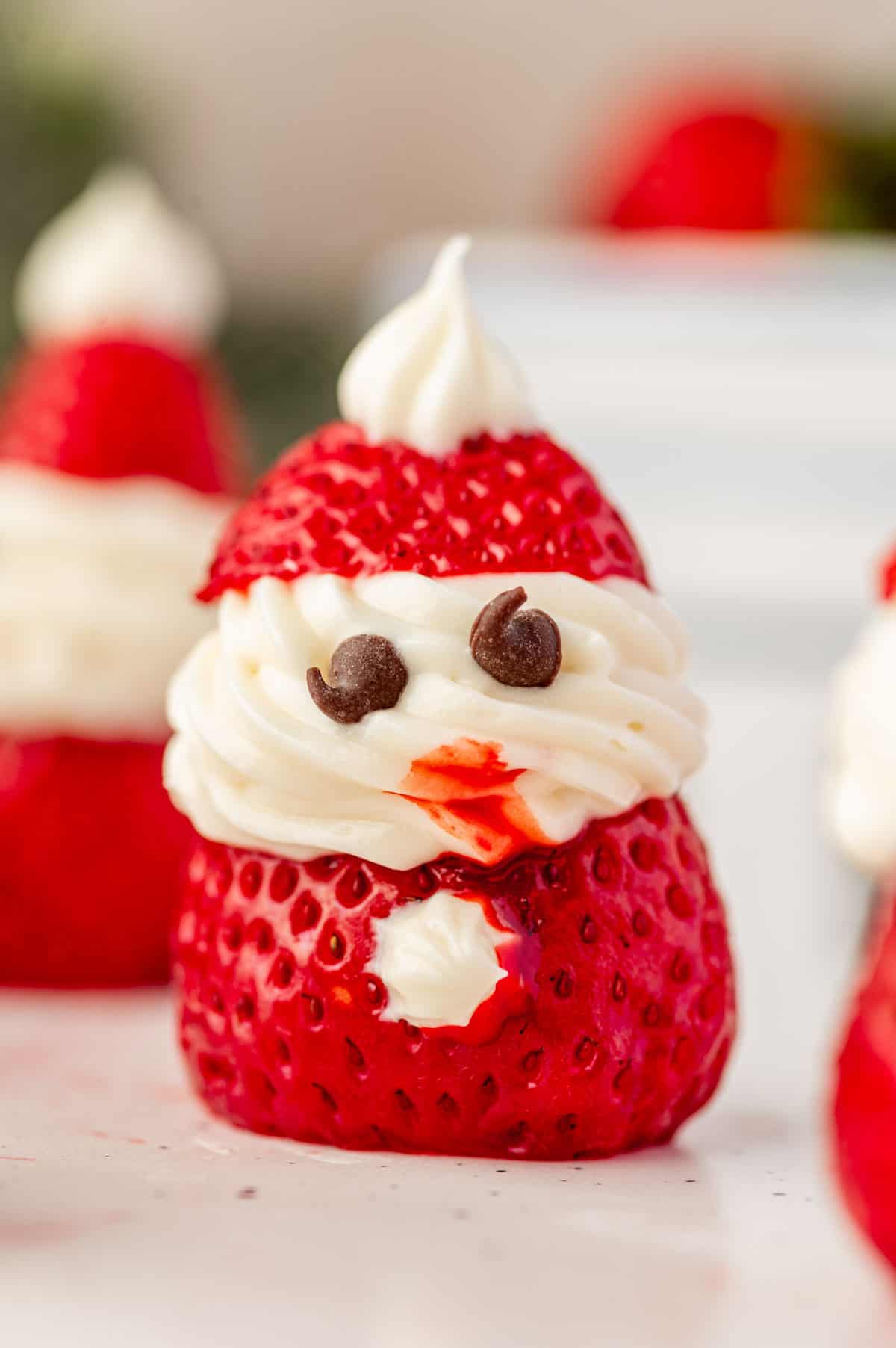 Close-up of a strawberry santa with Cool Whip filling and mini chocolate chip eyes, showing the top of each strawberry as Santa’s hat.