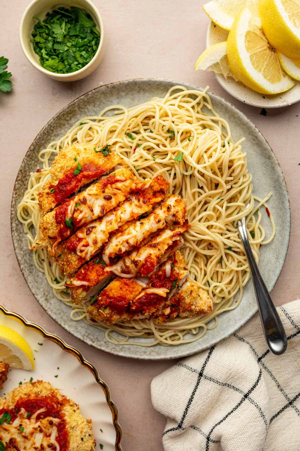 Twirling spaghetti topped with chicken parmesan sliced.