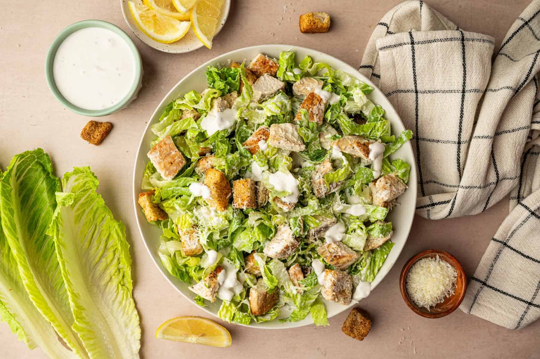 In a white bowl caesar chicken salad tossed with greek yogurt dressing.