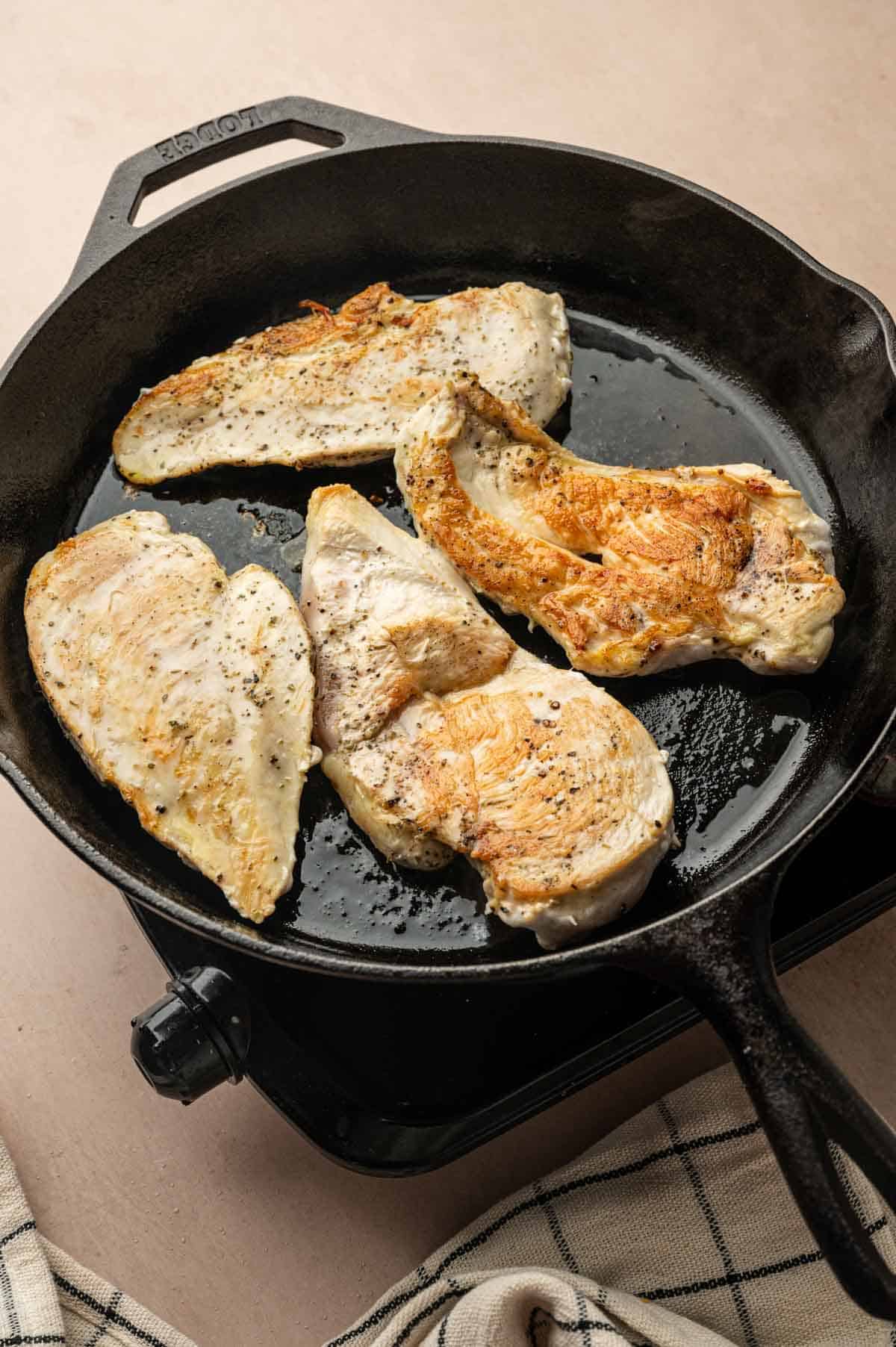 Chicken breasts being cooked in a cast iron skillet until golden brown
