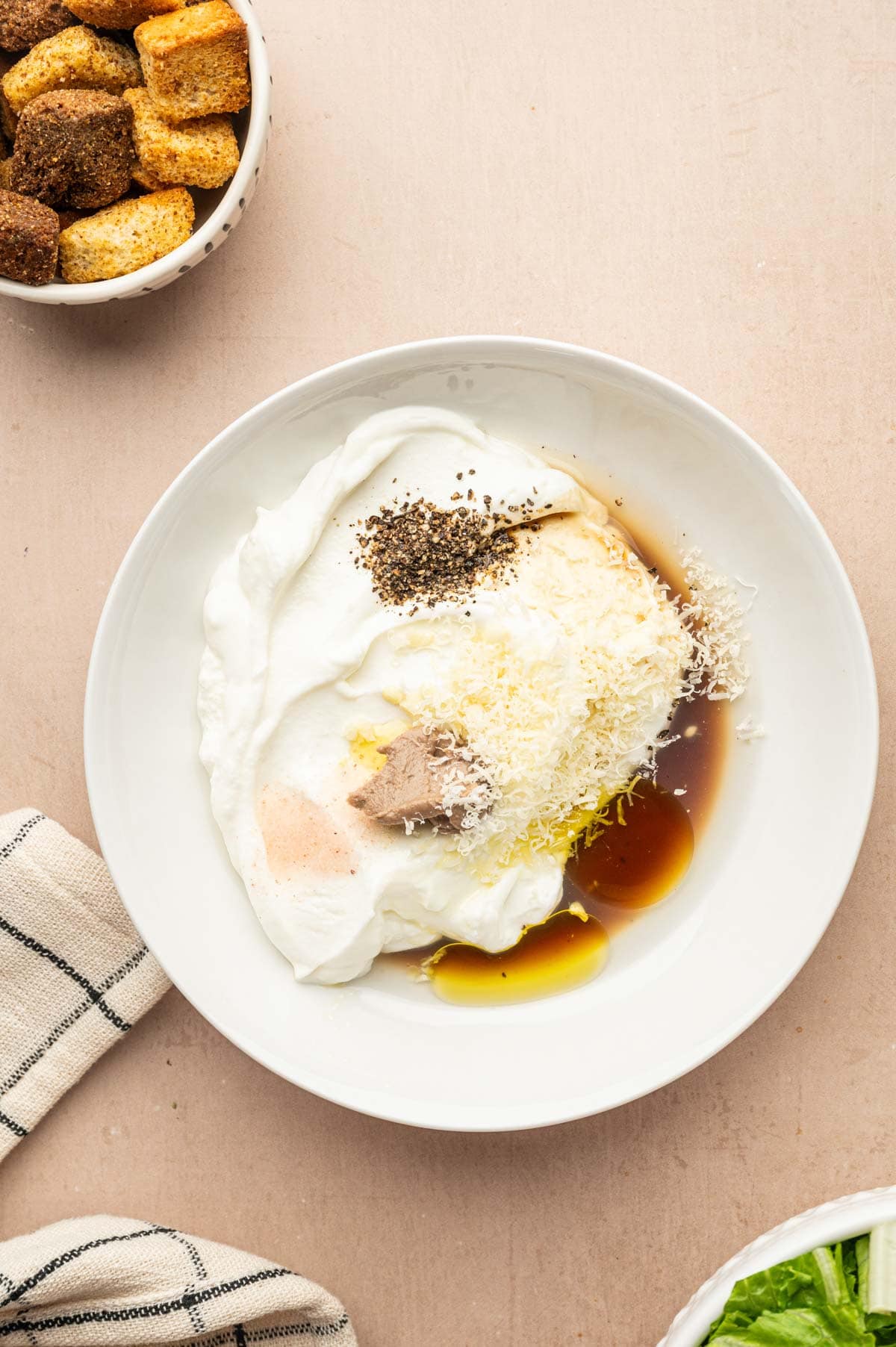 Greek yogurt Caesar dressing ingredients: yogurt, lemon, garlic, anchovy, Parmesan being mixed in a bowl.