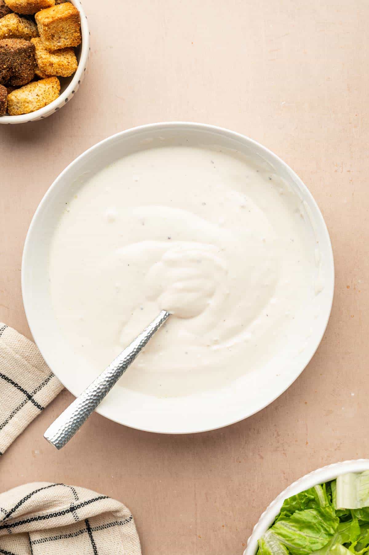 Whisking Greek yogurt Caesar dressing until smooth in a white bowl