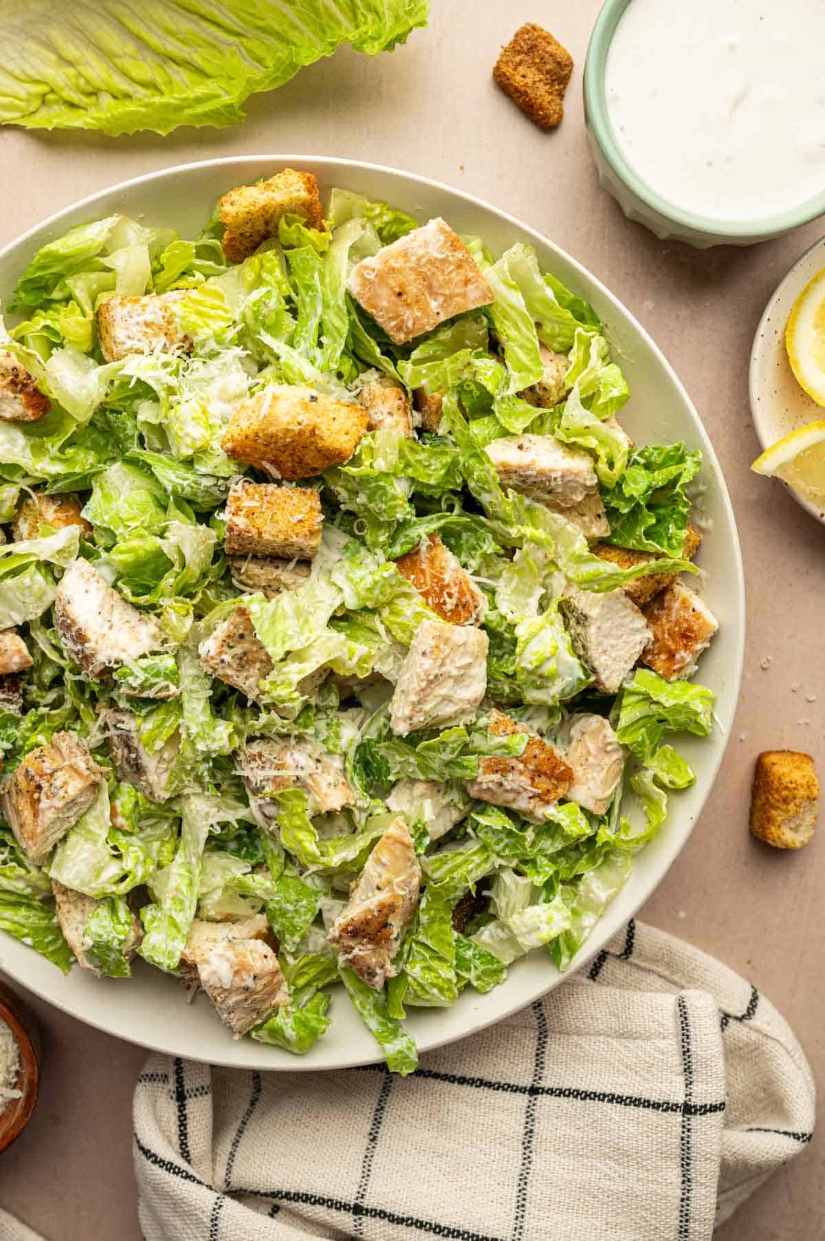 Overhead shot of Chicken Caesar Salad with crispy croutons and lemon wedges