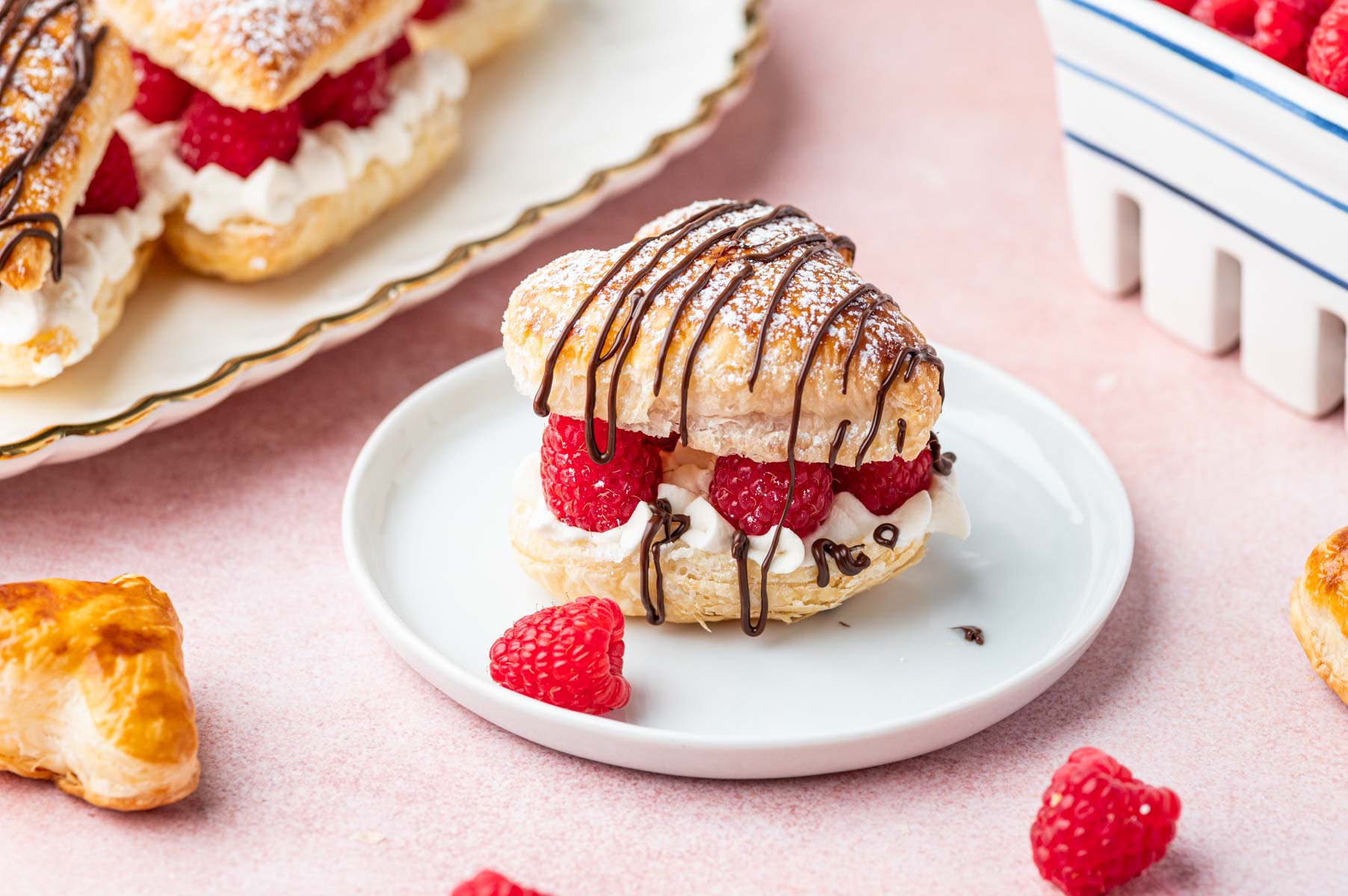 A white dessert plate with puff pastry hearts with raspberries.
