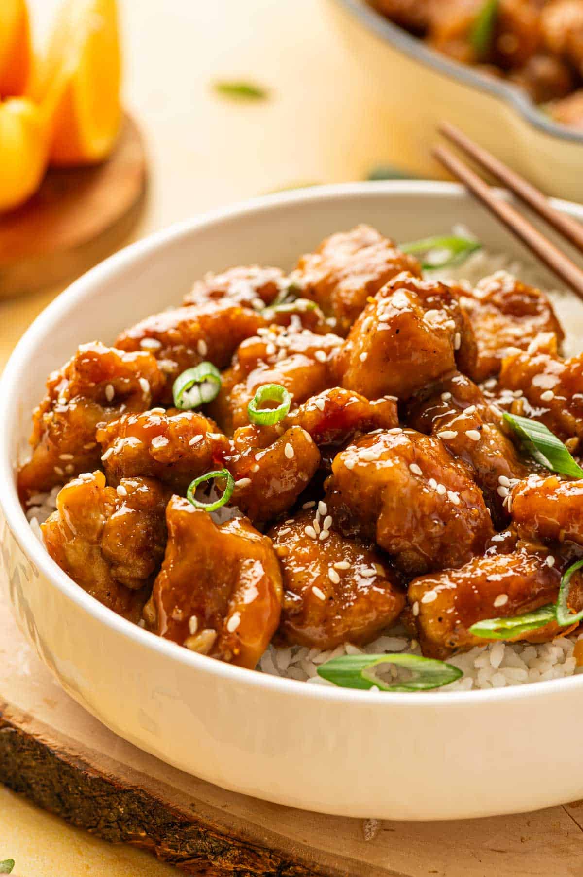 Orange chicken and rice in a serving bowl with fresh orange slices and garnishes