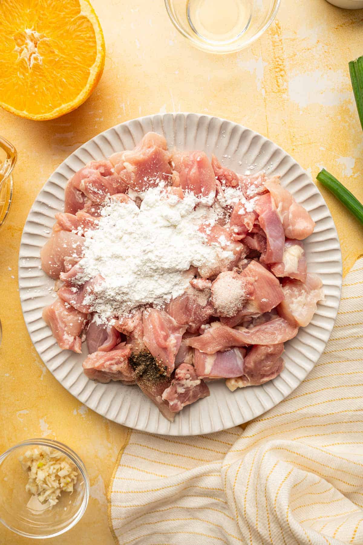 In a plate chicken pieces are being mixed with cornstarch, salt and pepper.