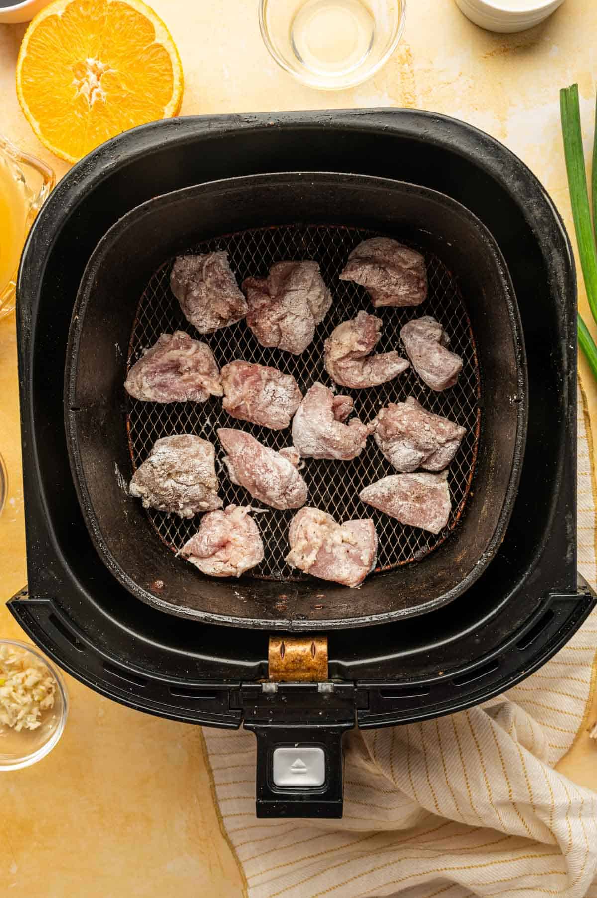 Flour coated chicken pieces are added to the air fryer basket.