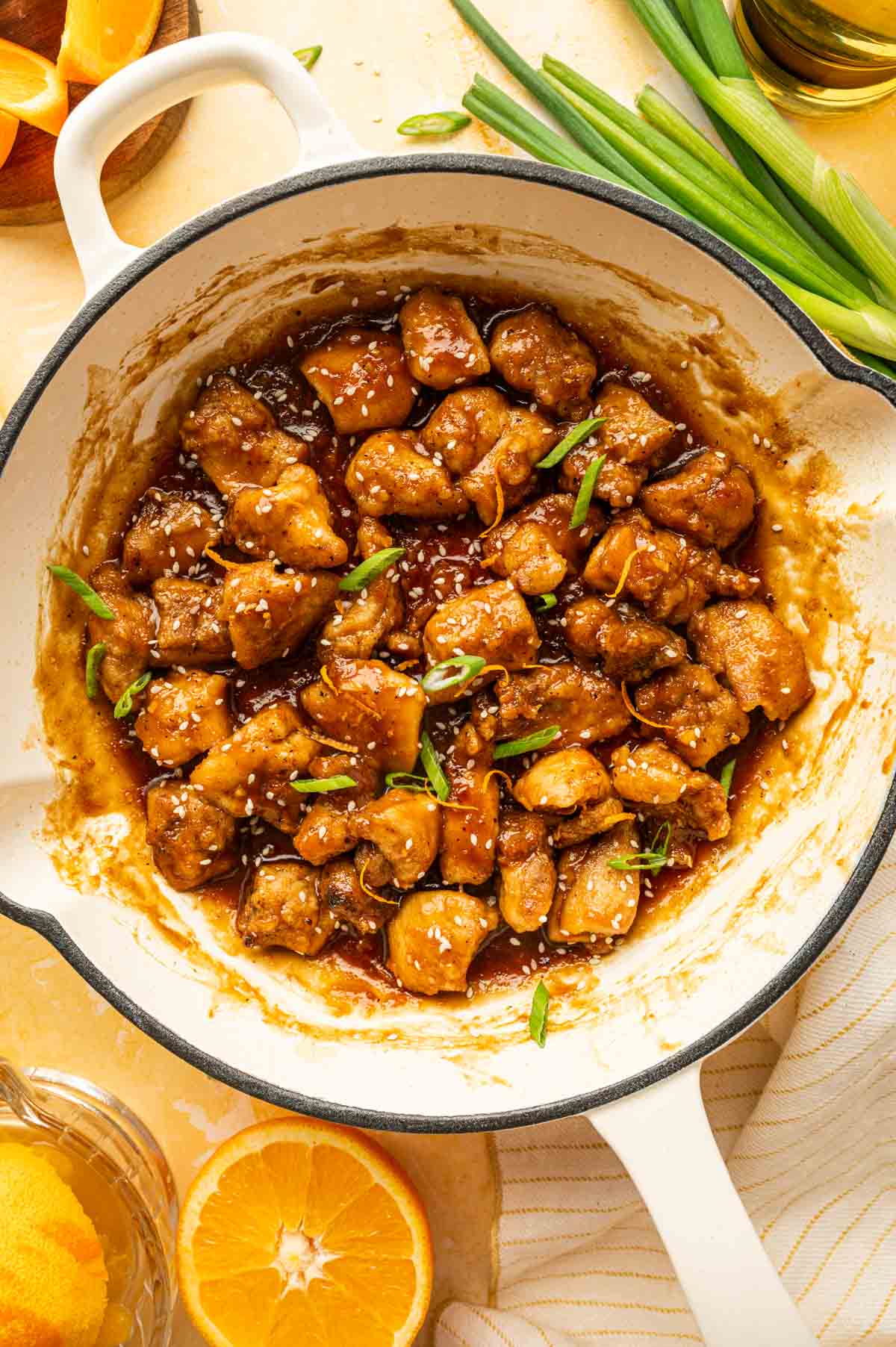 Air fried orange chicken in a white skilled garnished with sesame seeds and green onions.