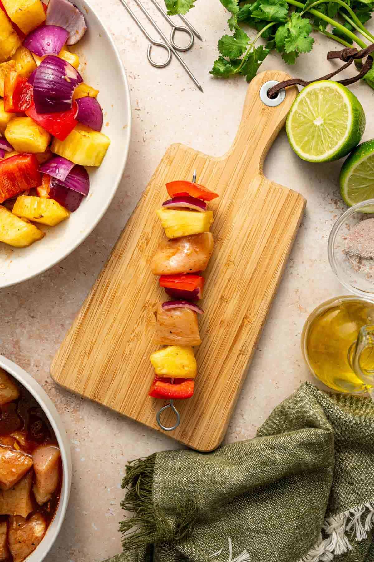 Chicken pieces, pineapple chunks, onions, red bell pepper being threaded in the skewers.