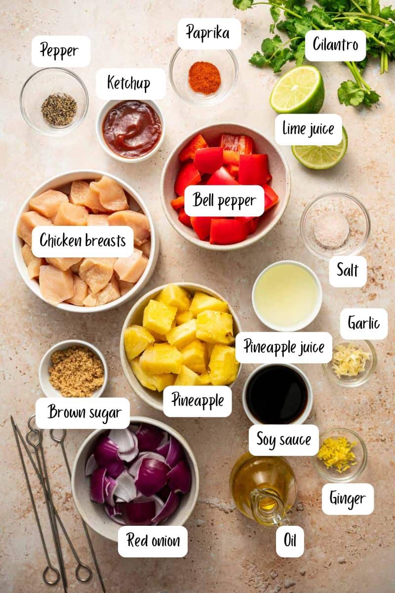 Overhead view of pineapple chicken kabobs ingredients placed along with fresh herbs and lime