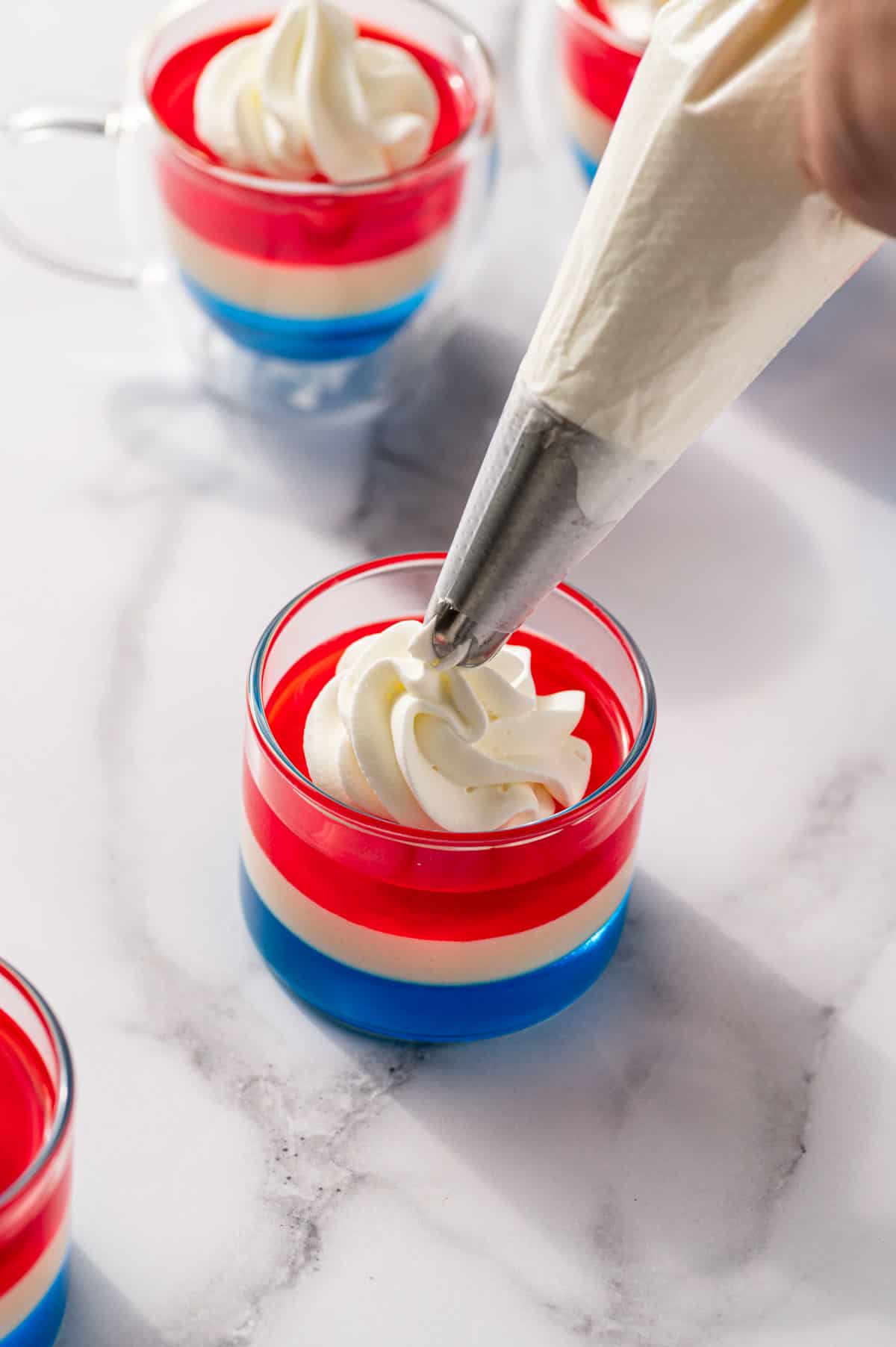 Red, white and blue jello shots being decorated with whipped cream.