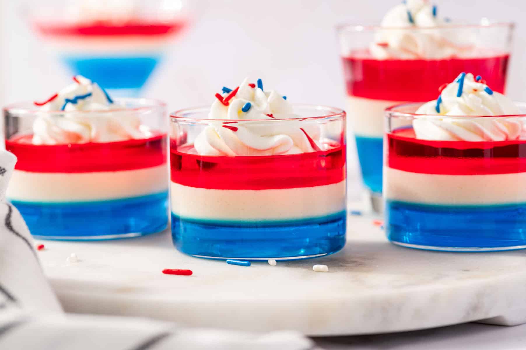 Red white and blue layered Jello shots in clear cups topped with patriotic sprinkles