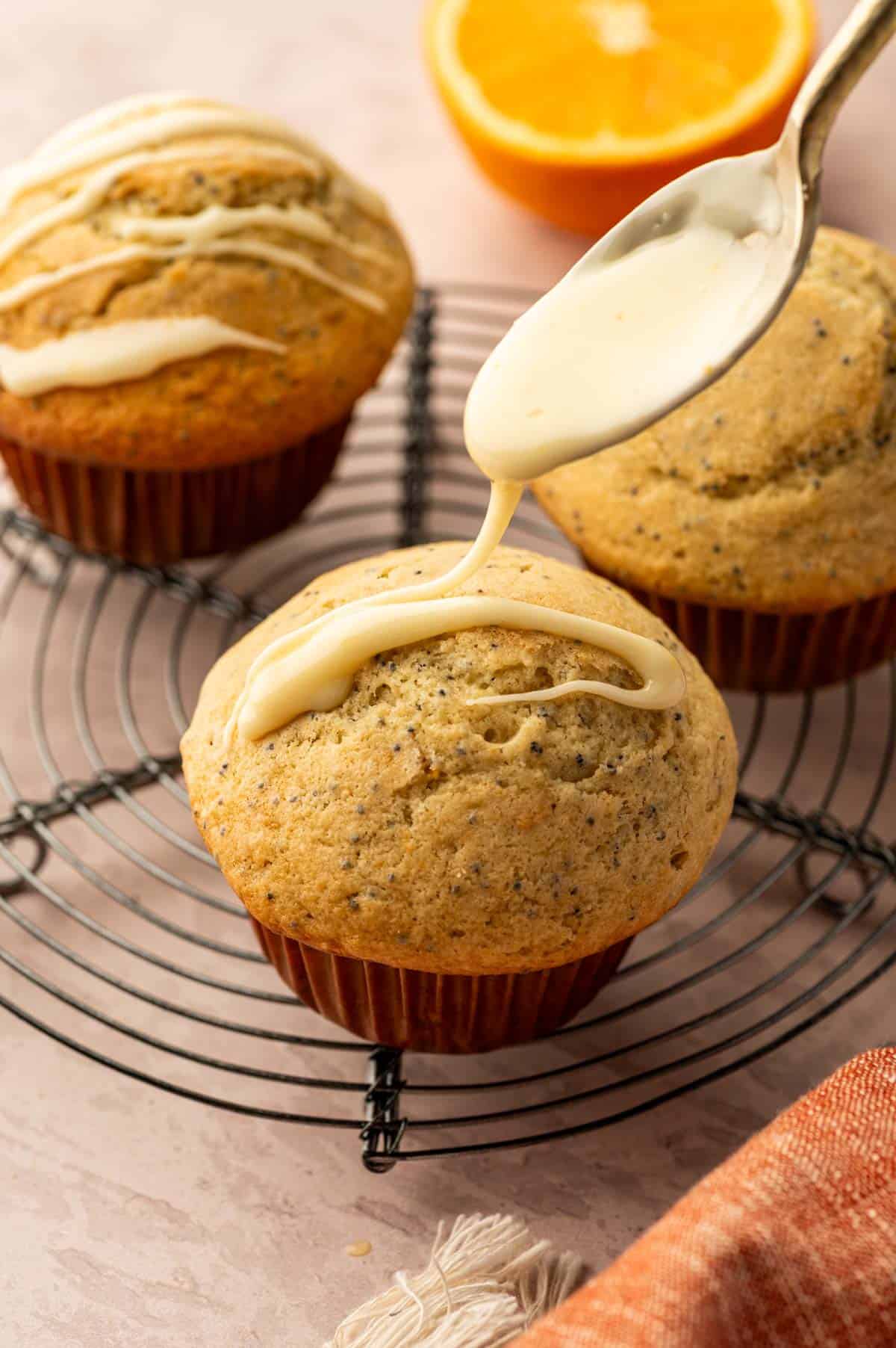 Orange icing being drizzled over the orange poppy seed muffins