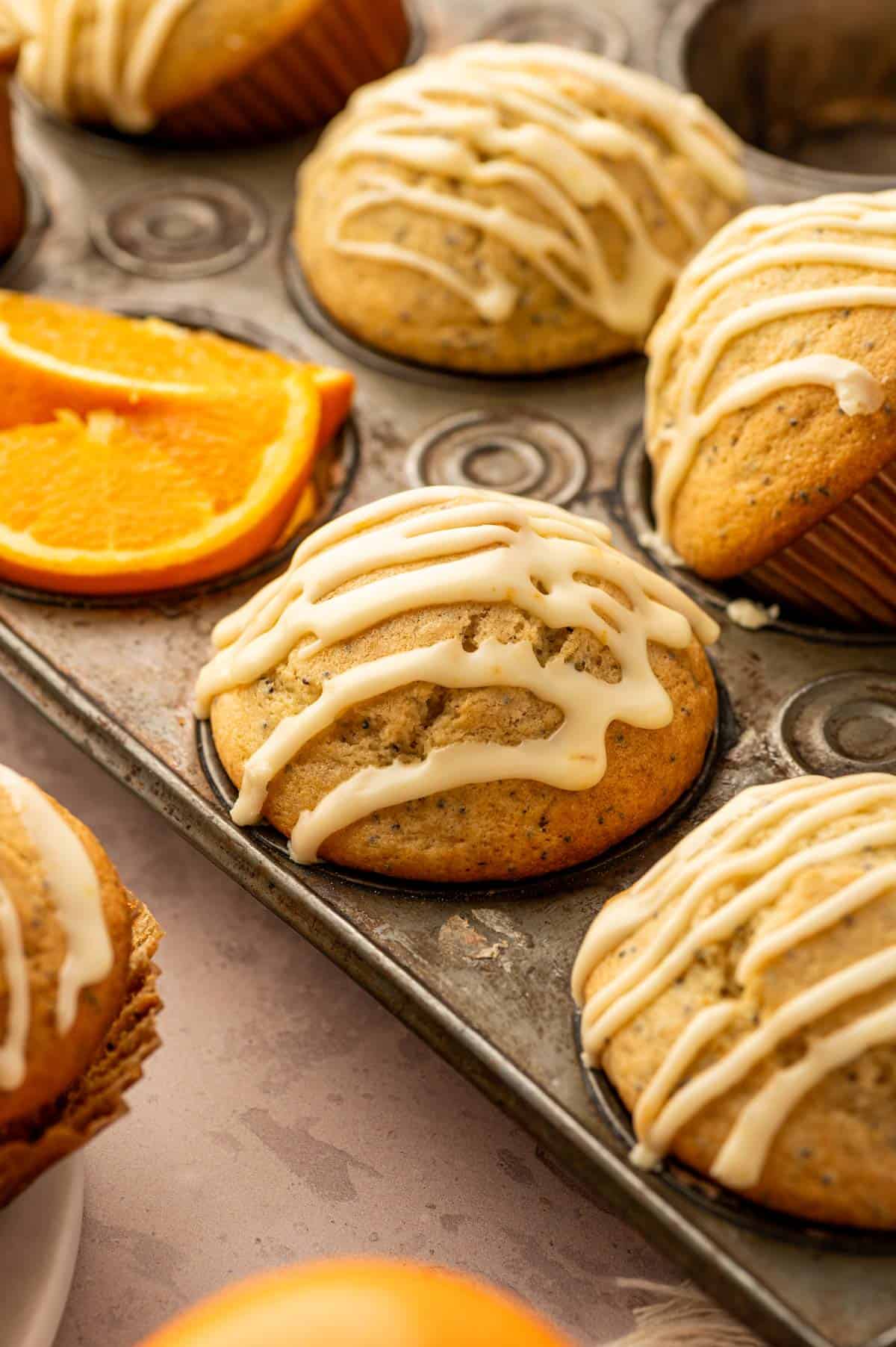 Orange poppy seed muffins with orange icing drizzle on a muffin pan